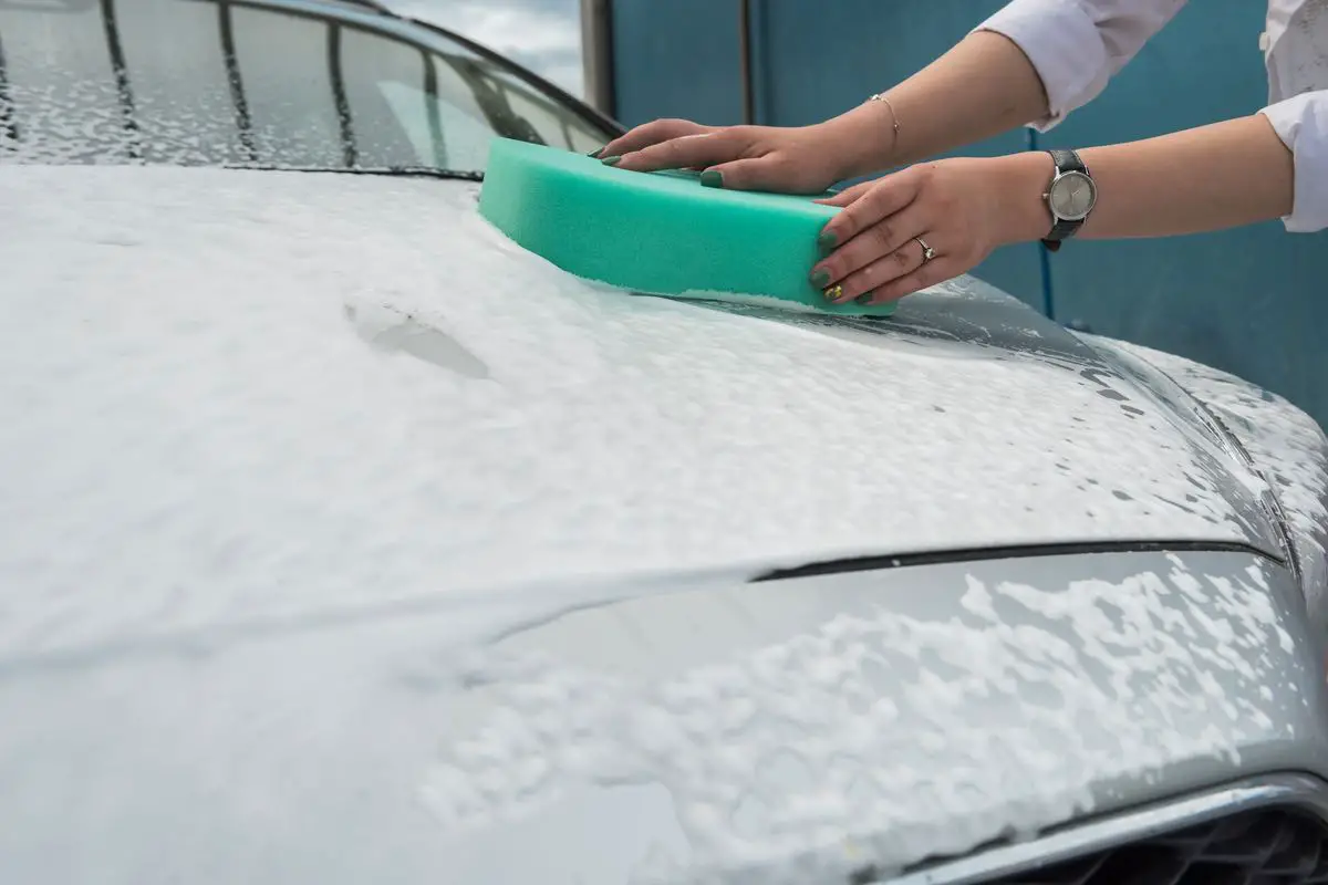 Female hands hold with green sponge and foam washing her car. Cleaning concept.